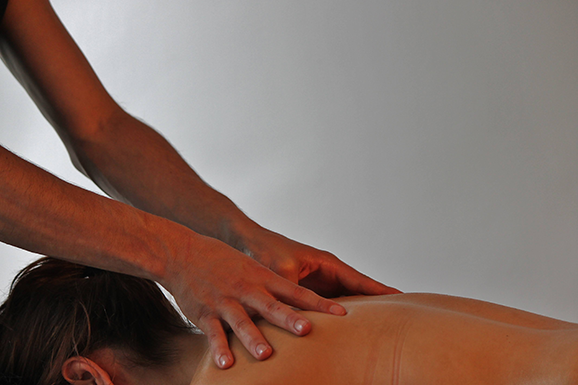 foto waarop we de handen van een masseur zien, die een relaxatiemassage geven in de nek/op de rug van een vrouw die op haar buik ligt